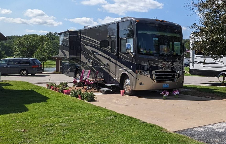 A Class-A motorhome on a concrete pad with flowers and a pond view at The Creeks