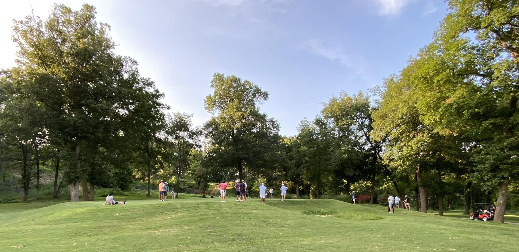 A lush tree-lined fairway with golfers and a red cart at The Creeks championship course