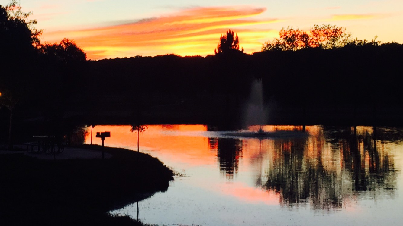 A fiery sunset reflected across the spring-fed pond and fountain at The Creeks